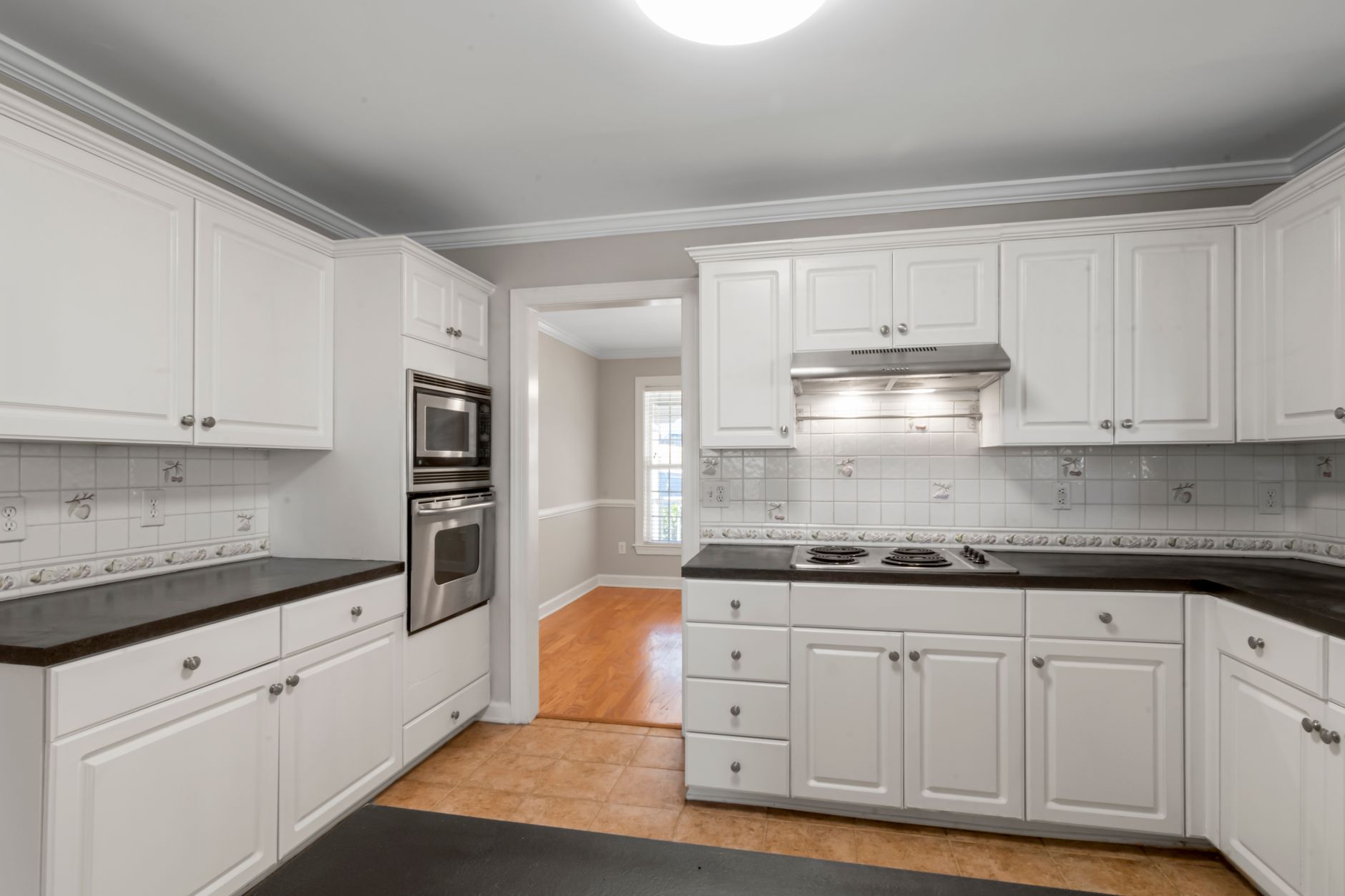 Dated U-shaped kitchen with white raised panel cabinets, dark counters and a wall oven, ready for a remodel